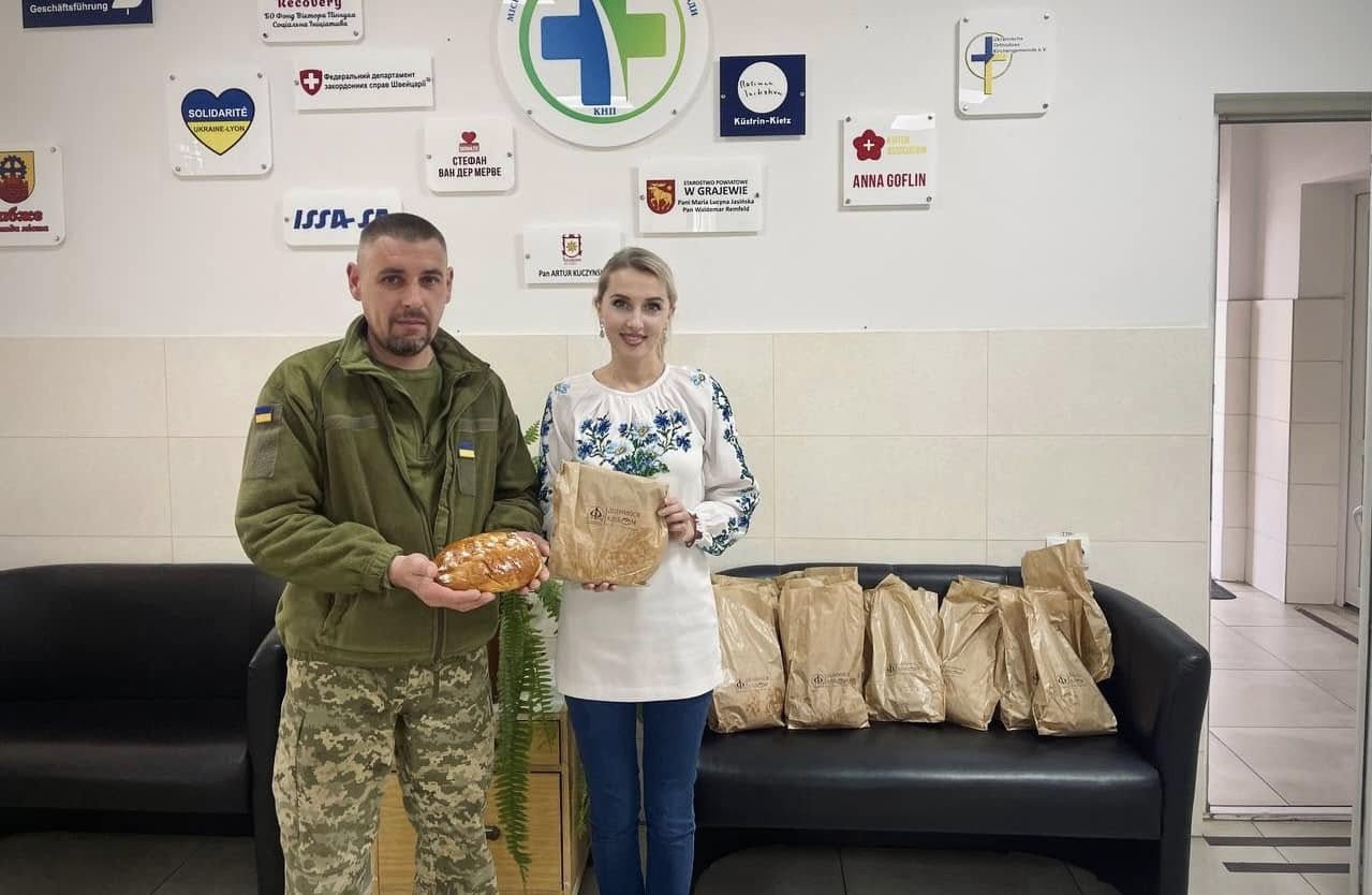 Жінка у вишиванці та чоловік у військовій формі позують з хлібом.